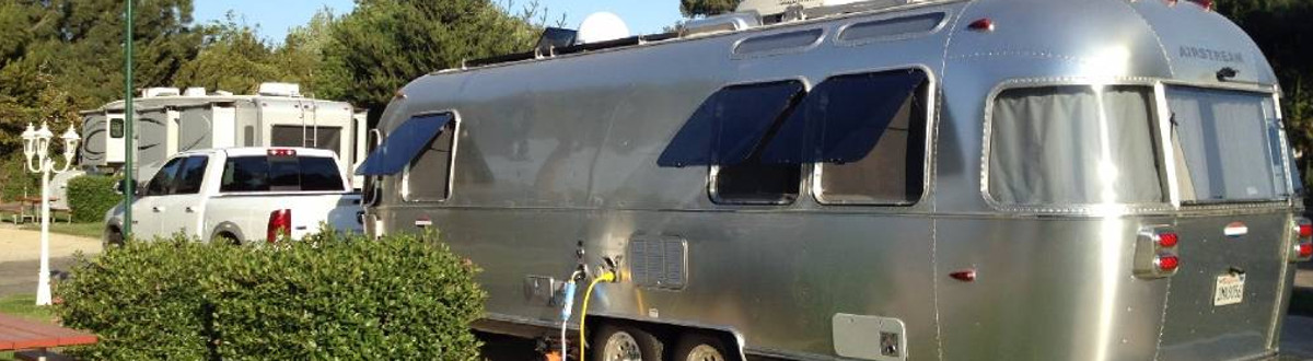 A white truck stationed in an RV park and attached to an Airstream® International Serenity 25 …
